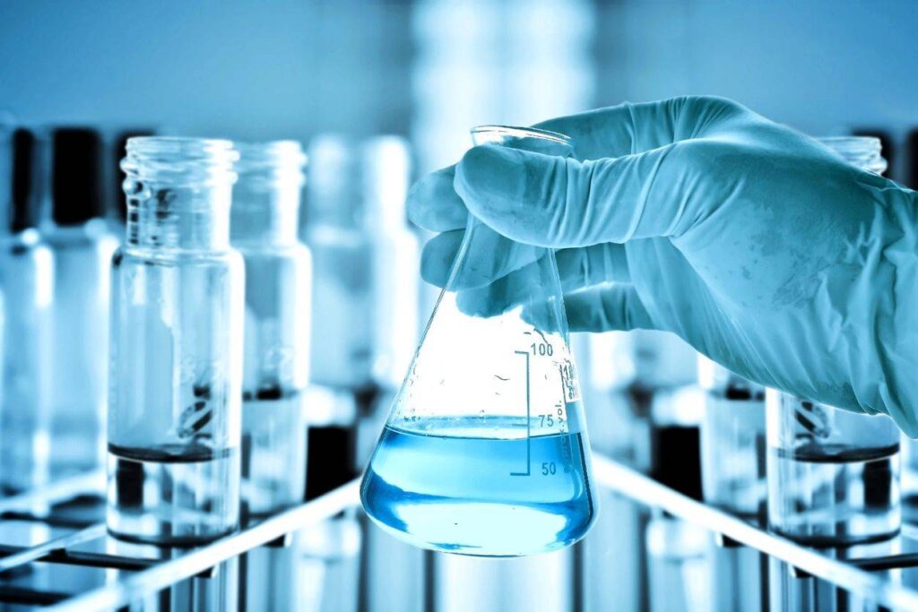 Gloved hand holding Erlenmeyer flask with blue liquid